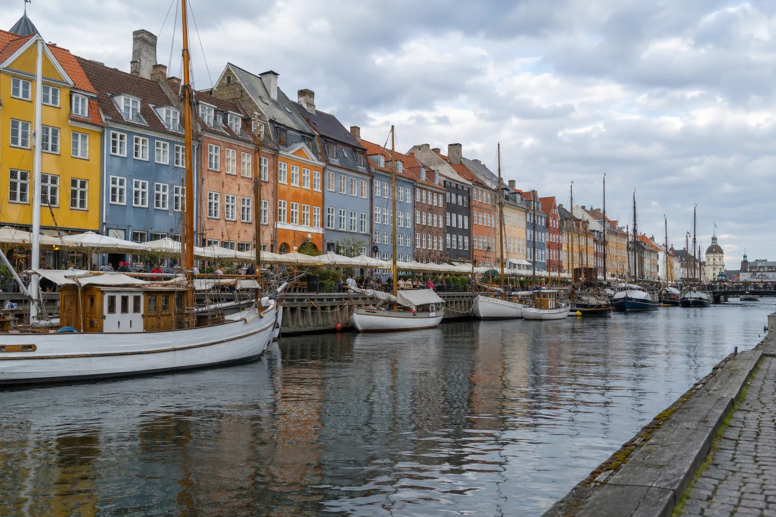 Kleurrijke gevels en houten boten langs Nyhavn onder een bewolkte lucht