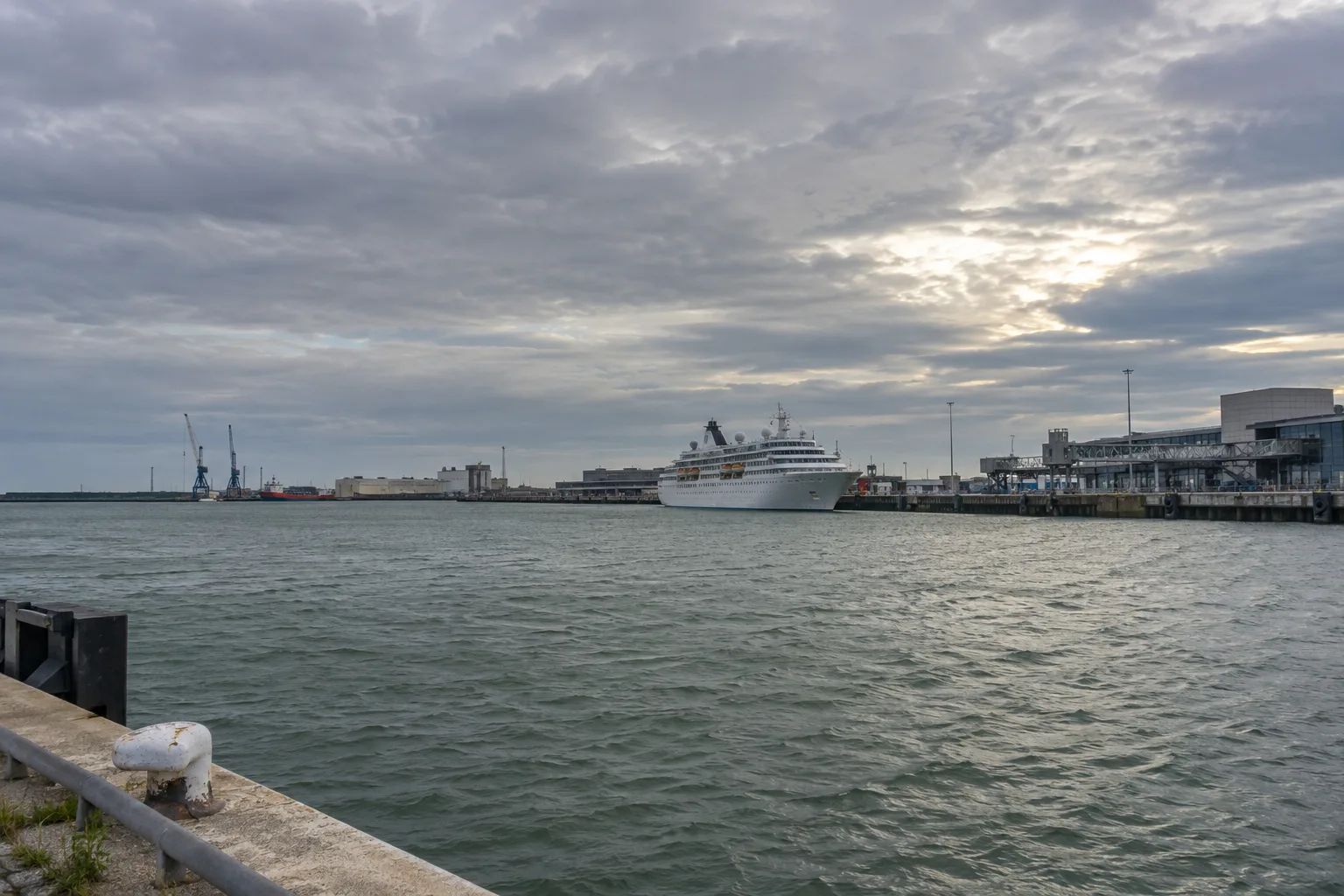 Een vlakke Nederlandse zeehaven met een passagiersschip in de verte